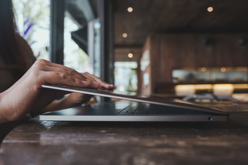 Closeup image of hands close or open laptop on wooden table in office with blur bokeh background