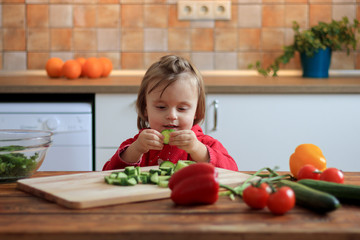 Cute baby girl eating healthy vegetables at kitchen