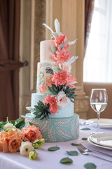 Home wedding for-tiered cake on the table in the restaurant decorated with pink roses and green leaves in a rustic style