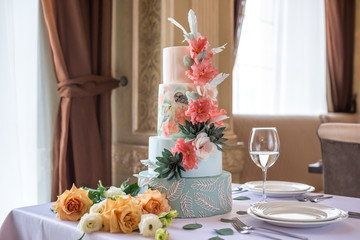 Home wedding for-tiered cake on the table in the restaurant decorated with pink roses and green leaves in a rustic style