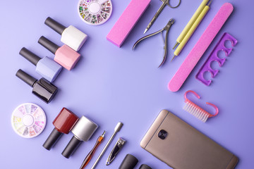 Set of cosmetic tools for manicure and pedicure on a purple background. Gel polishes, nail files and clippers, top view