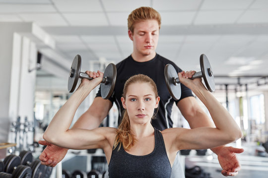 Trainer hilft junger Frau beim Hanteltraining