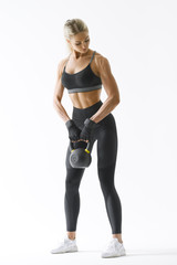 Caucasian fitness model working out with kettlebell in black sportswear Full length shot of young muscular female bodybuilder doing heavy kettlebell exercise for deltoids