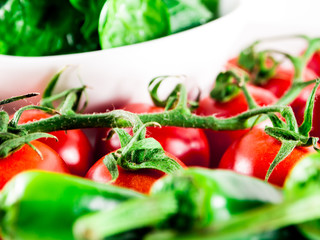 Little branch of cherry tomatoes, bowl of spinach, green hot peppers and garlic in plate over white isolated background.