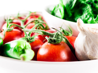 Little branch of cherry tomatoes, bowl of spinach, green hot peppers and garlic in plate over white isolated background.