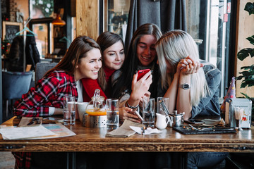 four friends look at the phone and laugh