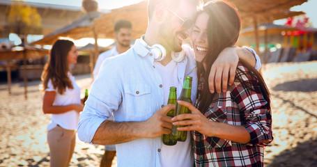 Happy young couple drinking beer and having fun at the beach