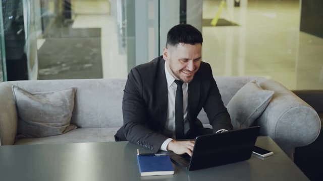 Successful Caucasian businessman in formal clothes smiling, clapping and rubbing his hands while recieving good news using laptop compute in classy cafe