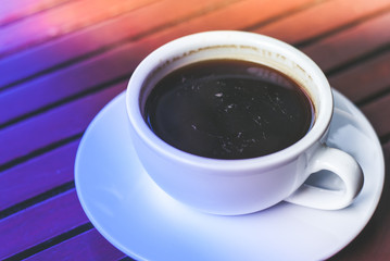 A cup of hot espresso coffee on plate on wooden table in morning rush time with colorful lighting