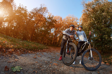 Fototapeta premium Happy young couple going for a bike ride on an autumn day in the park, backlight.