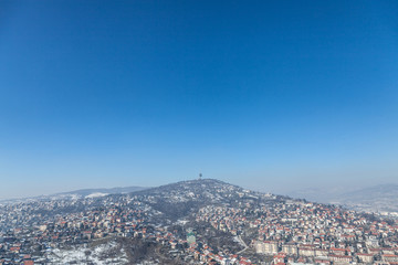 Aerial view of the hills of the suburbs of Sarajevo, Bosnia and Herzegovina during a cold winter afternoon snow covering everything. The TV Tower of the city can be seen in background.