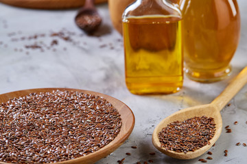 Flax seeds in bowl and flaxseed oil in glass bottle on light textured background, top view, close-up, selective focus