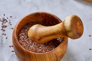 Top view close-up picture of wooden pestle and mortar with flaxseeds on light background, shallow depth of field