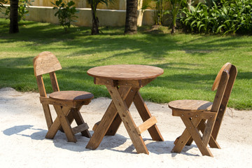 Table and wooden chairs in tropical garden next to the sea on the sand beach, Thailand. Close up