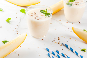 Summer fruits, refreshing drinks. Vegan food. Breakfast. Smoothie of yogurt, raw organic yellow melon, flax seeds and mint. With striped straws, in glasses, white marble table, copy space