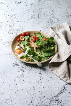 Vegetarian sandwiches with avocado, poached egg, spinach, cherry tomatoes on whole grain toast bread on ceramic plate with textile napkin over white marble background. Copy space