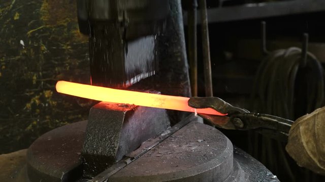Using pneumatic hammer to shape hot metal. Clouse up man's hand making the sword out of metal.