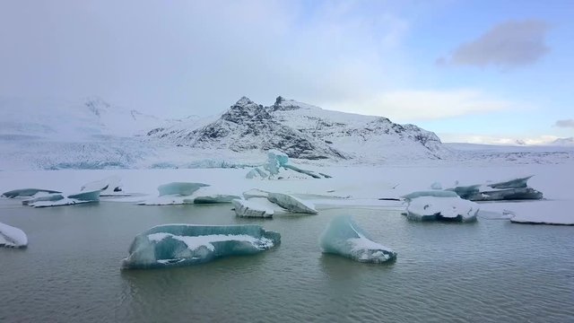 Aerial view of Icebergs along the shore of Jokulsarlon glacial lagoon during a blue overcast day.
