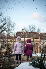 Obraz premium Two little girls in the countryside watching a flock of birds in the sky
