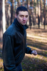A young man of criminal appearance in a black leather jacket posing in an autumn forest.