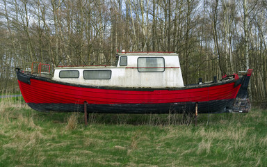 Laesoe / Denmark: Side view of an old boat on jacks on a wild meadow in springtime