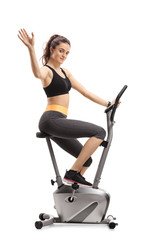 Fototapeta na wymiar Fitness woman working out on an exercise bike and waving at the camera