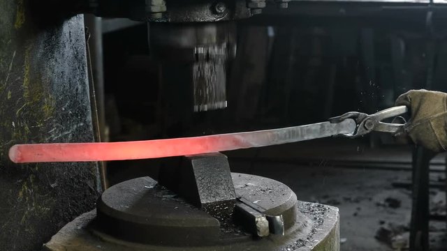 Making the sword out of metal at the forge. Closeup man's hand using pneumatic hammer to shape hot metal
