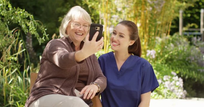 4K Happy senior lady & young nurse, posing for selfie in the garden on a sunny day. Slow motion