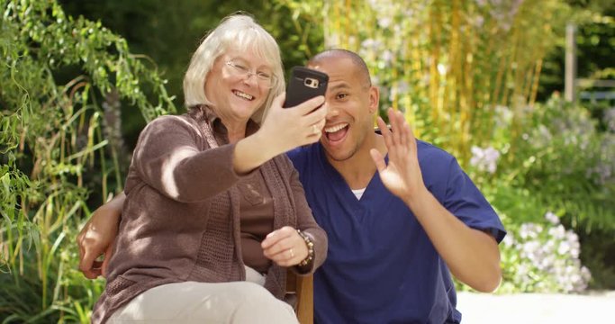 4K Happy senior lady & male nurse, posing for selfie in the garden on a sunny day. Slow motion