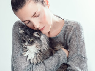 Stylish, young woman gently hugging her kitten on a white background. People, pets, care