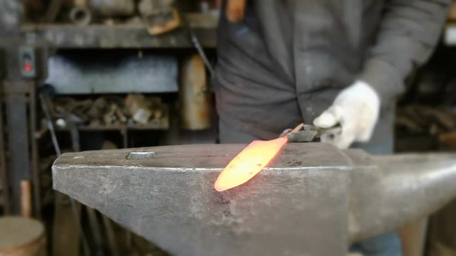 Making the knife out of metal at the forge. Close up blacksmith's hands taking a hammer and hitting hot metal on an anvil.