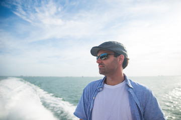 Man wearing a hat and sunglasses looking into distance on boat