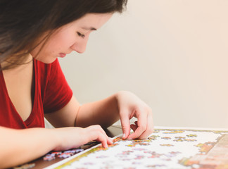 Fototapeta premium Woman trying to match pieces of a Jigsaw Puzzle Game. Playing the game, side view.