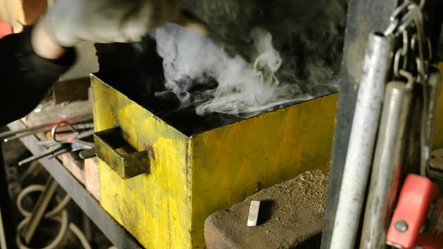 Hardening of the knife blade in a special solution. Close-up of the man's hands dip the knife blade in oil.