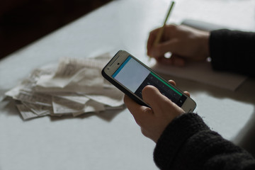 Male hand using smartphone and calculating monthly fees. Financial concept.
