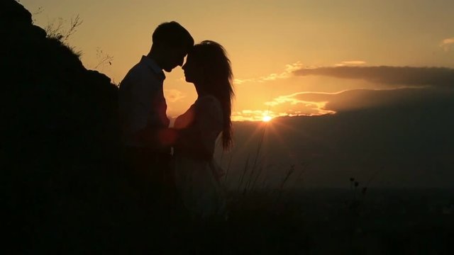 Romantic view of the couple silhouette tenderly hugging and standing head-to-head during the beautiful golden sunset.