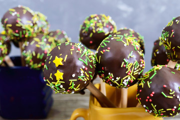 Holiday cake pops, decorated with white and black chocolate in cups on a wooden background. Candy on a stick. Close up