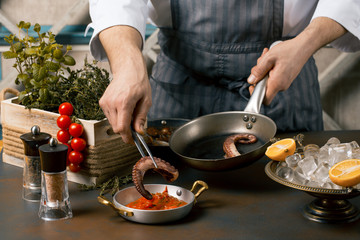 Fototapeta na wymiar Chef cooks spreadsheets octopus tentacles. Chef lays octopus on tomato sauce. Gourmet Restaurant