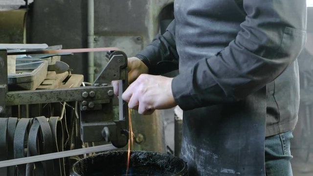 Grinding billets of metal on a belt-grinding machine. Close-up of a man's hand.
