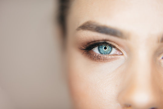 Close-up shot of beautiful blue eye of the attractive fresh woman with natural make-up at beige background. Part of healthy face.