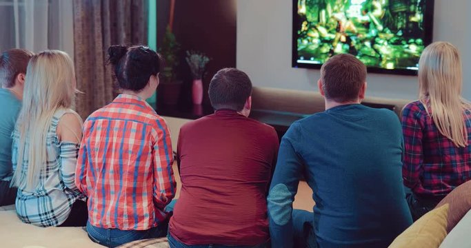 Company of the friends enjoy relaxing on couch playing videogames and having fun in modern flat