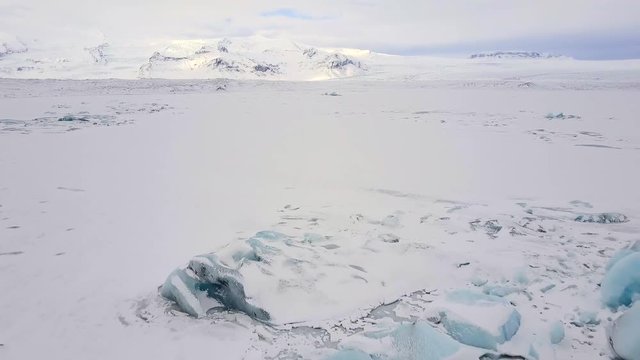 Aerial footage of beautiful winter landscape. Snow covered glacier lake viewed from air. Dramatic frozen countryside in Iceland.