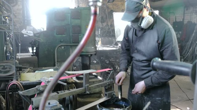 Grinding billets of metal knife on a belt-grinding machine. Worker performs his job in a protective mask on his face in the shop among the equipment