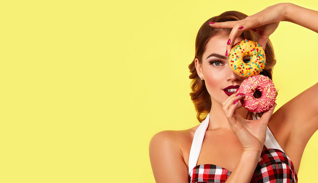 Beautiful young bright girl in retro style holds two bright donut in hands.Fashion, beauty, makeup, retro, pin-up, cosmetics, dessert, delicious, advertising, bright, magazine, postcard, hairdo.