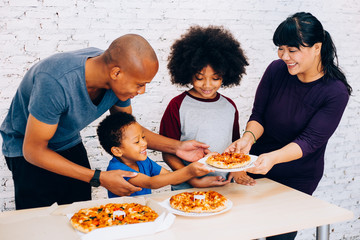 Fototapeta na wymiar Happy family of African American parents and little boy and girl having pizza together happily at home. Family and parenthood concept