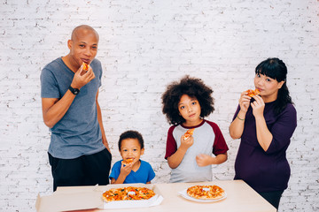 Happy family of African American parents and little boy and girl having pizza together happily at home. Family and parenthood concept