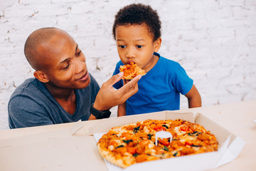 African American father feeding his cute son with pizza. Warm family concept. Warm family, Father and son relationship