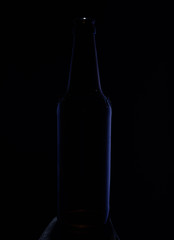 Close-up image. Bottle on a dark background with  blue glare on the sides of the glass.