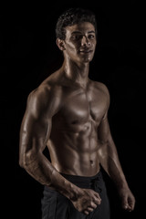 Fototapeta na wymiar Highly retouched fitness model and bodybuilder. Looking and smile. Posing chest, biceps and six pack abs. Concept of power and self-confidence. black background.
