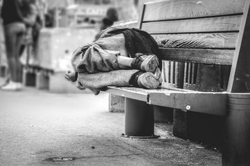 Poor homeless man or refugee sleeping on the wooden bench on the urban street in the city, social...